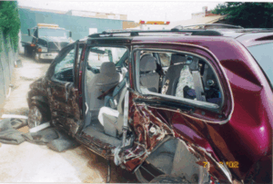 This picture shows the driver's side of the Harty's red van after the crash; there is extensive damage from the ground up to the bottom of the windows and from the front bumper all the way back to the rear tire.